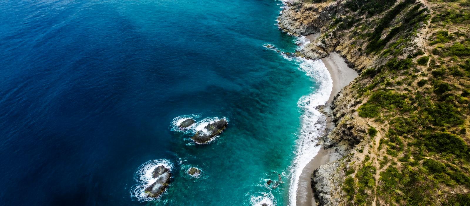Aerial drone photo of turquoise ocean surf meeting a rugged coastline